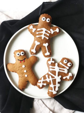 3 gingerbread men decorated as a mummy, skeleton and vampire on a white plate