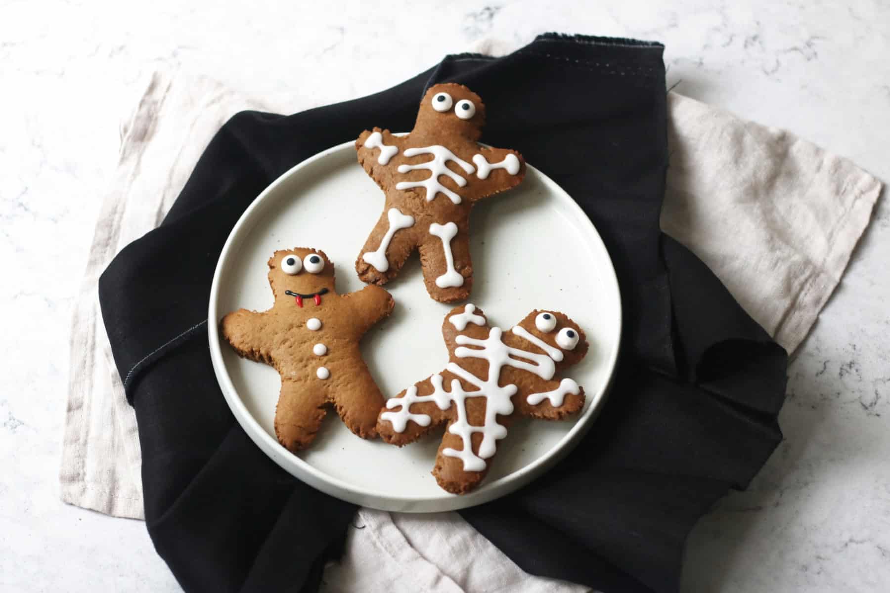 3 gingerbread men decorated as a mummy, skeleton and vampire on a white plate