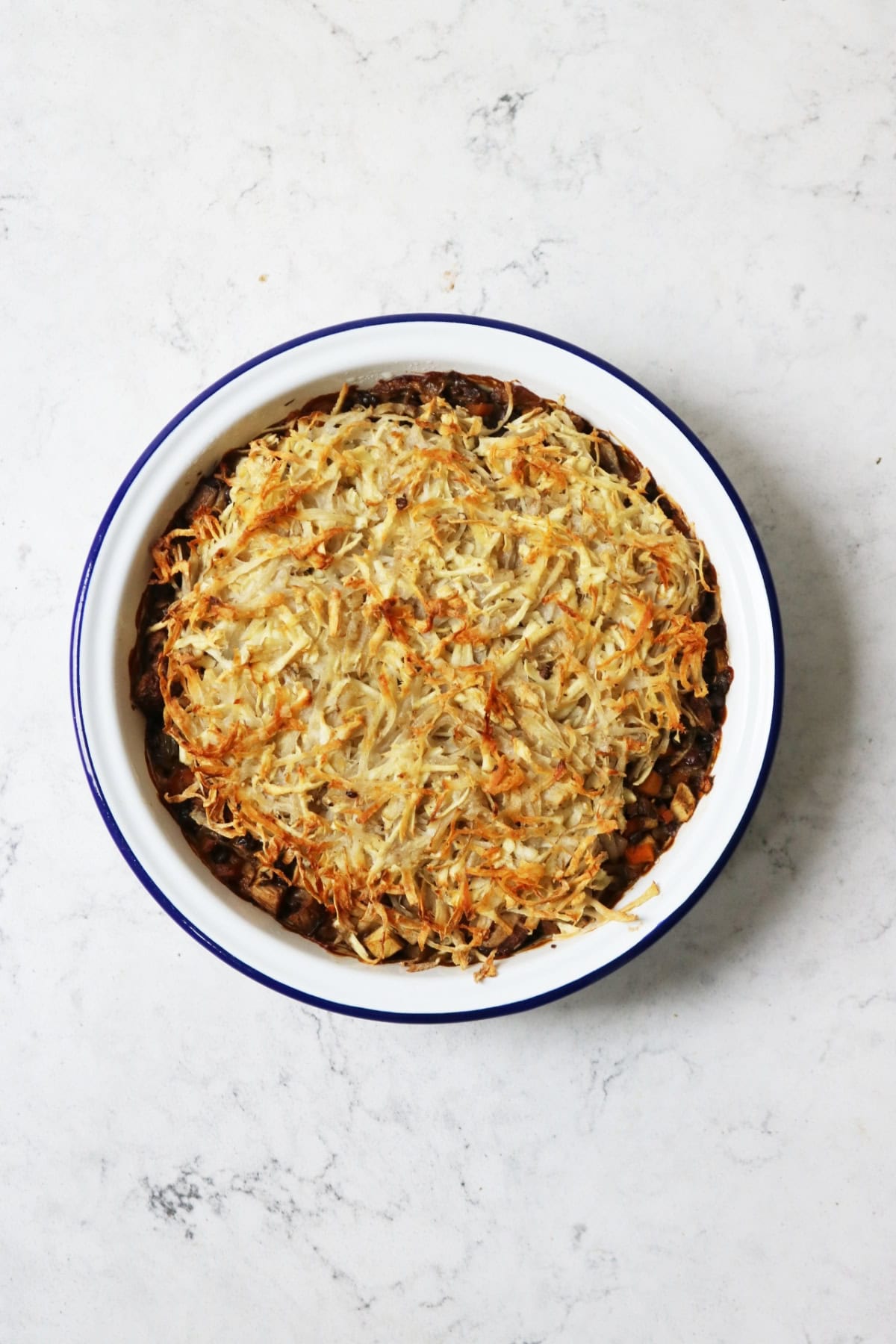 Cooked Rösti-Topped Puy Lentil and Mushroom Pie cooling on a white marble counter top