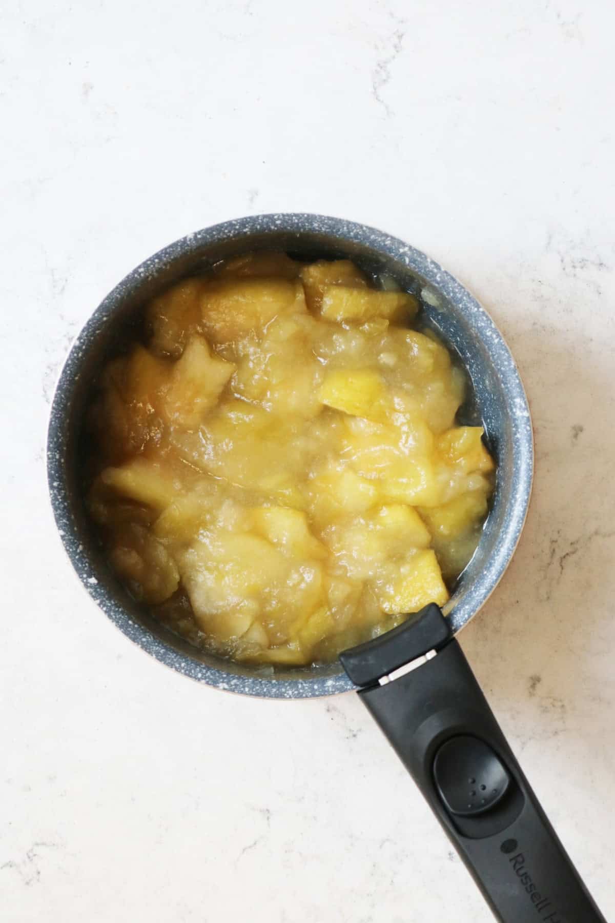 Cooked apple, cardamom and rose compote cooling in a saucepan