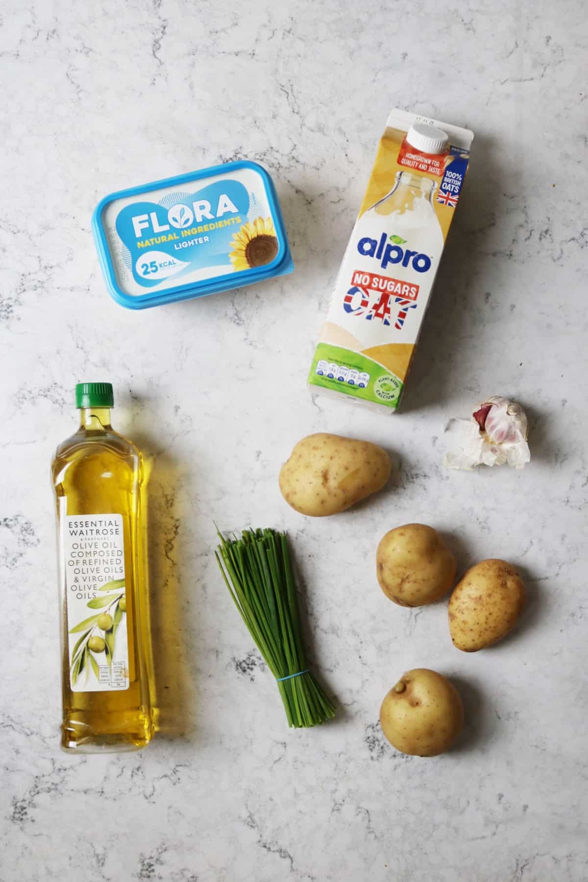 Vegan butter, plant milk, olive oil, chives, potatoes and garlic on a white marble counter top