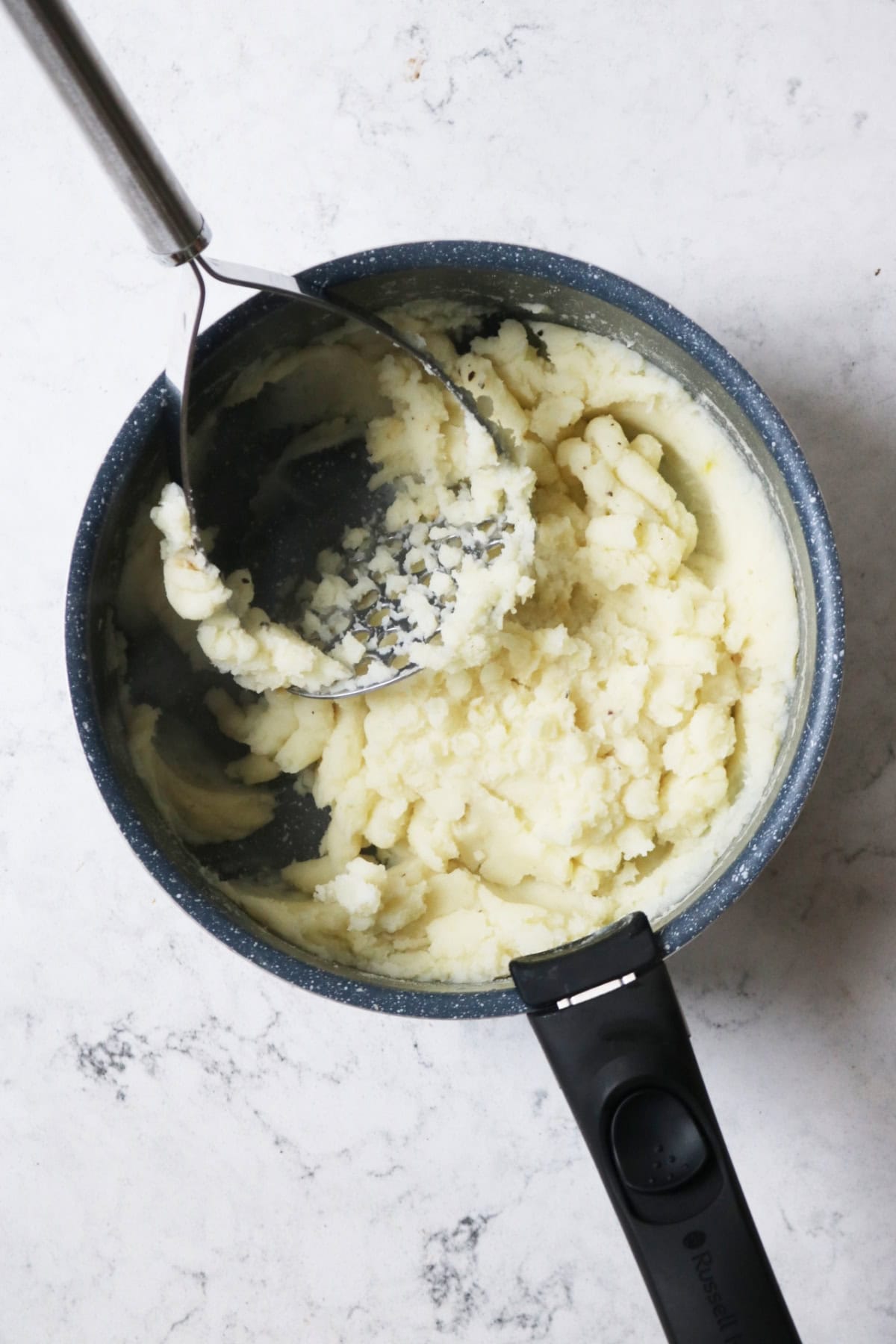 Mashed potatoes in a saucepan with the potato masher