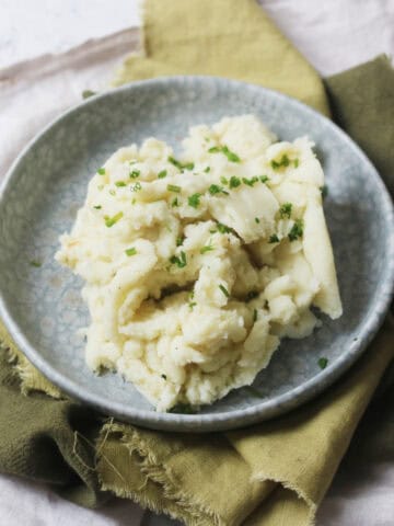Vegan Garlicky Mashed Potatoes topped with Chives on a blue plate