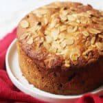 A baked Vegan Panettone topped with flaked almonds served on a white plate with a red napkin