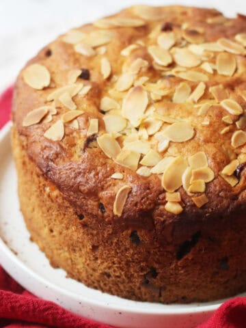 A baked Vegan Panettone topped with flaked almonds served on a white plate with a red napkin