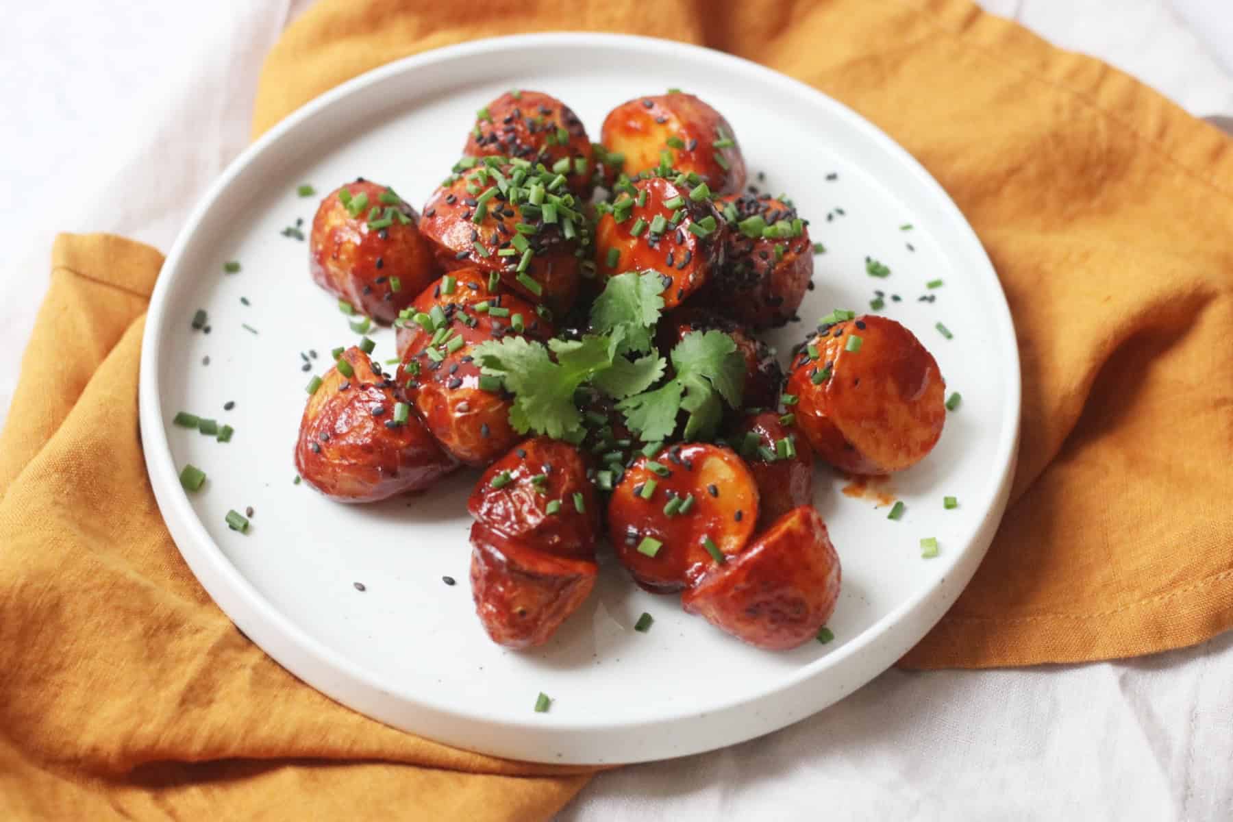 A plate of Crispy Gochujang Potatoes topped with sesame seeds, chives and coriander.