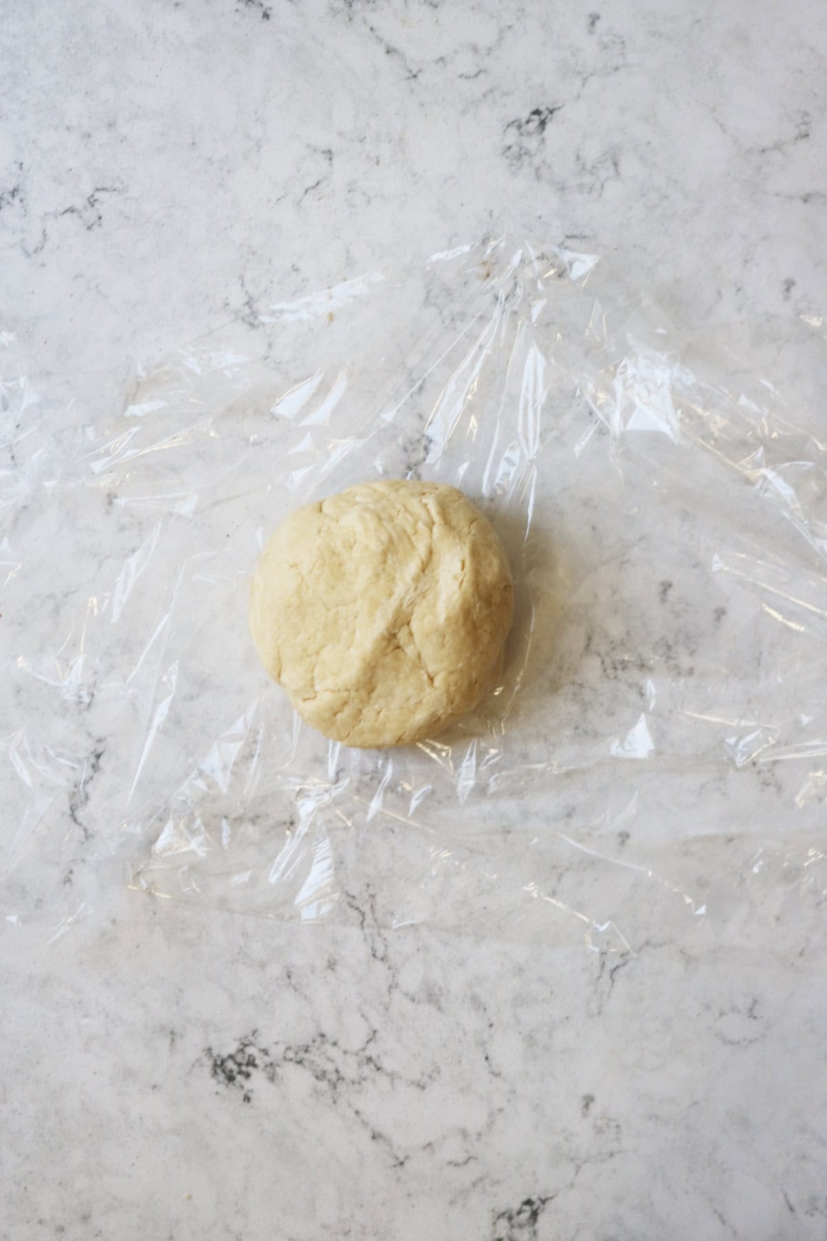 A ball of shortcrust pastry dough that has been wrapped in clingfilm and chilled in the fridge