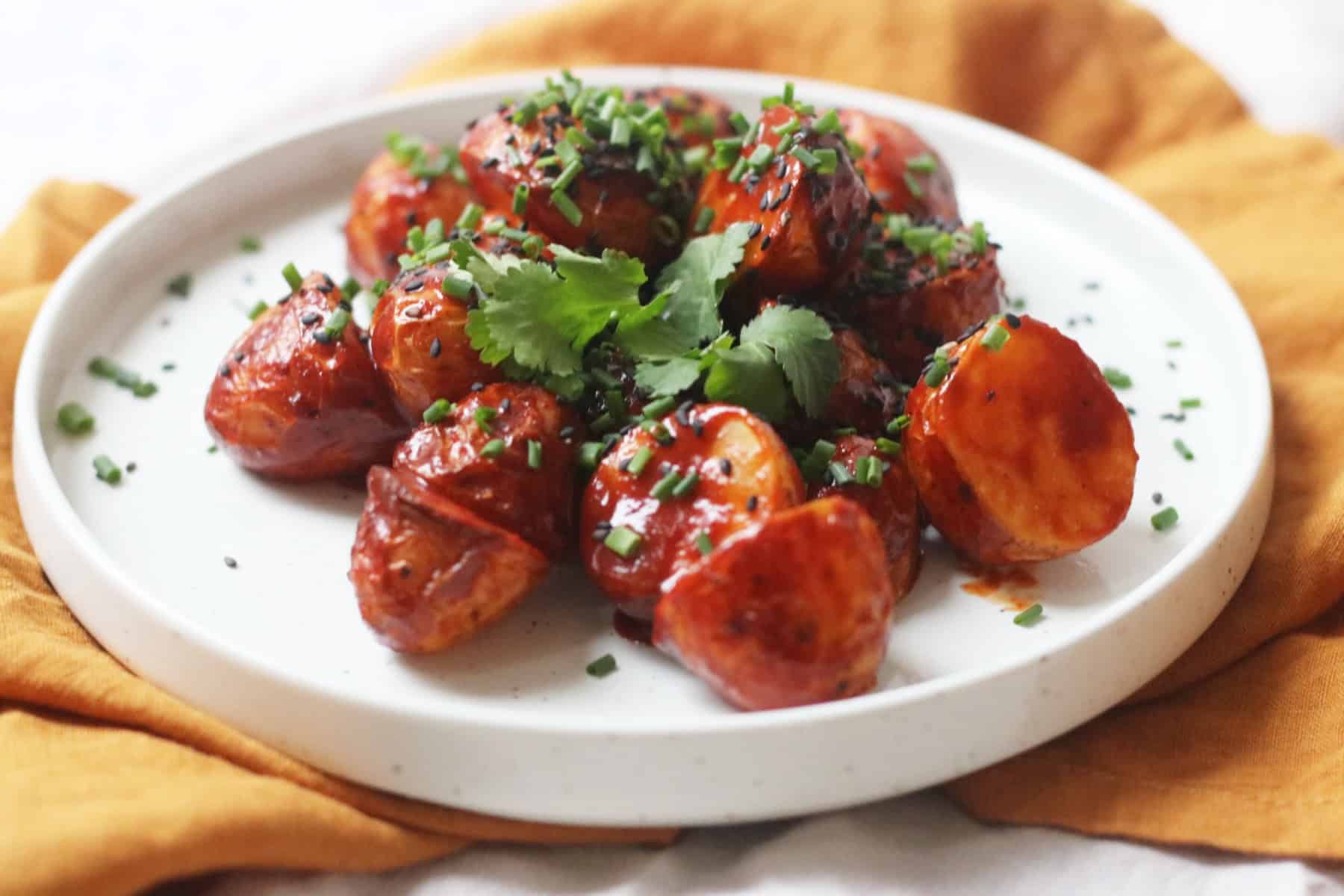 A plate of Crispy Gochujang Potatoes topped with sesame seeds, chives and coriander.