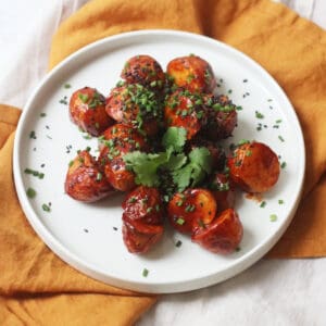 A plate of Crispy Gochujang Potatoes topped with sesame seeds, chives and coriander.