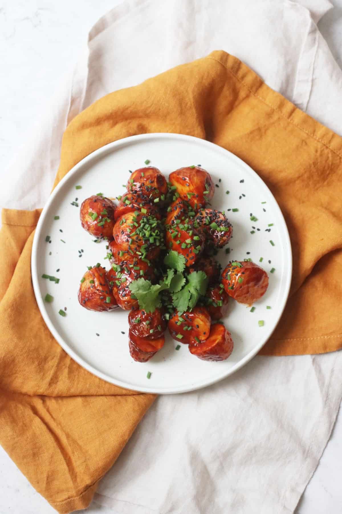 A plate of Crispy Gochujang Potatoes topped with sesame seeds, chives and coriander.