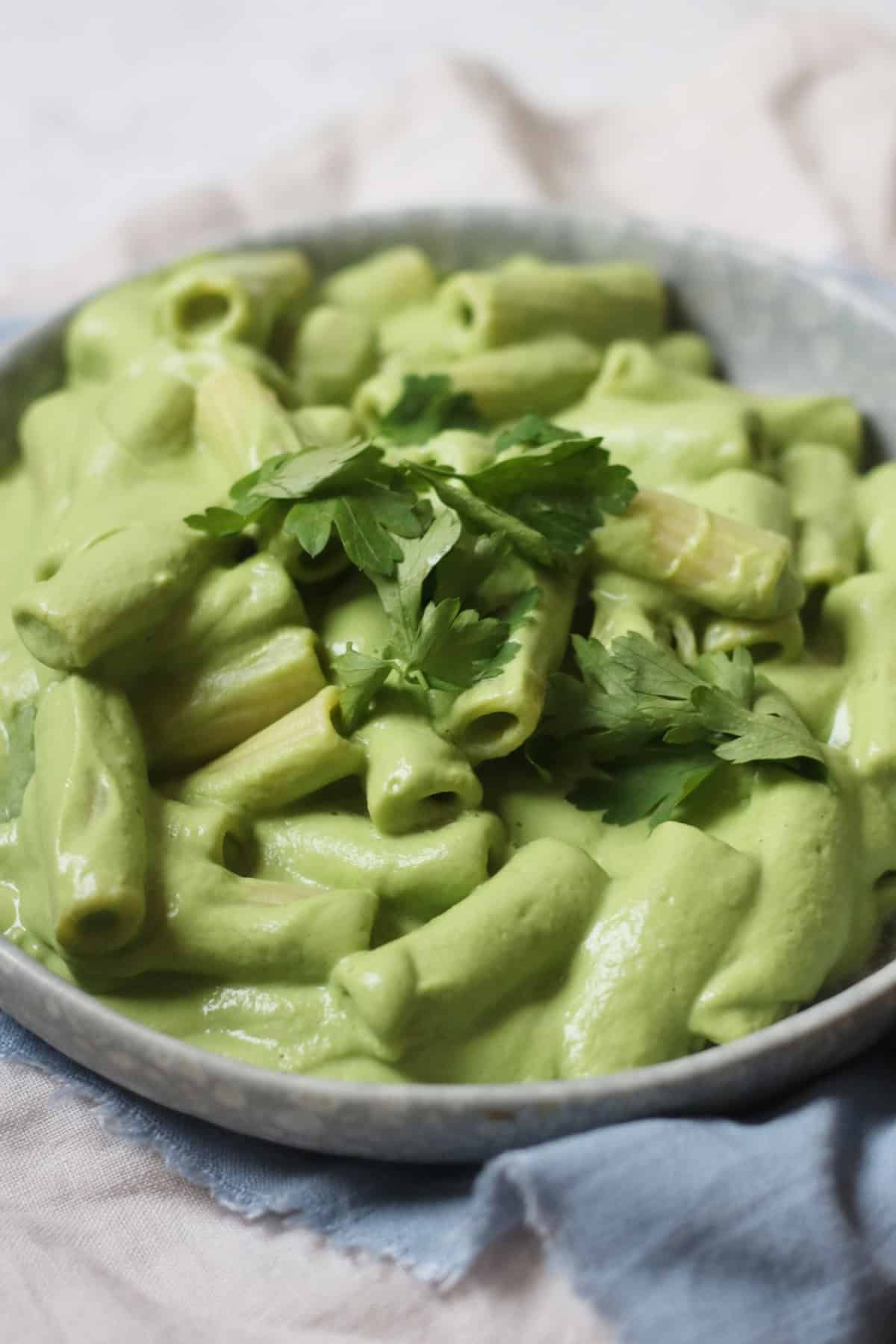 A plate of pasta made with Vegan Creamy Broccoli Pasta Sauce and garnished with parsley sat on top of a blue napkin with a knife and fork