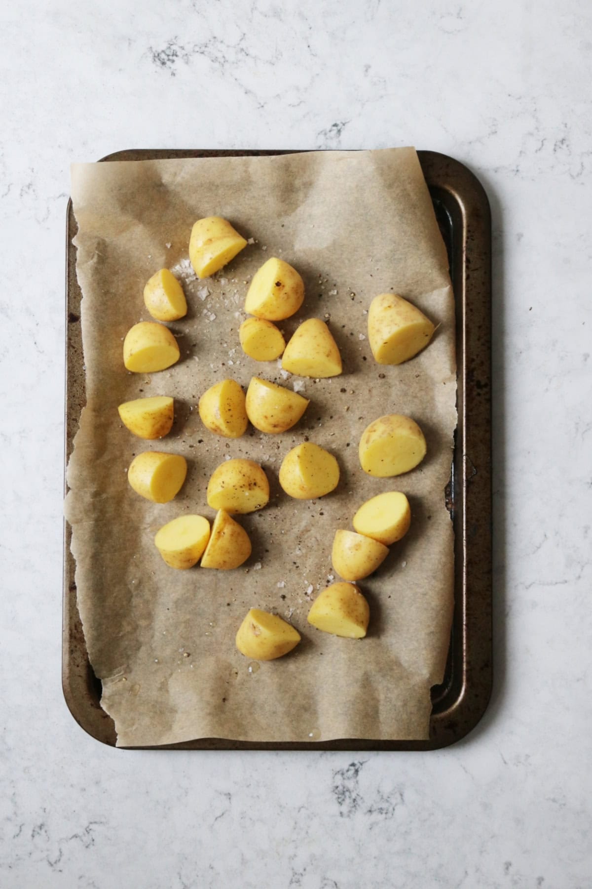 Baby potatoes cut in half on a baking tray with salt and pepper, ready for the oven