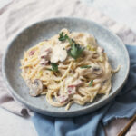 A plate of vegan carbonara topped with parsley, served on a blue plate