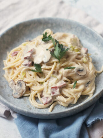 A plate of vegan carbonara topped with parsley, served on a blue plate