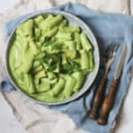 A plate of pasta made with Vegan Creamy Broccoli Pasta Sauce and garnished with parsley sat on top of a blue napkin with a knife and fork