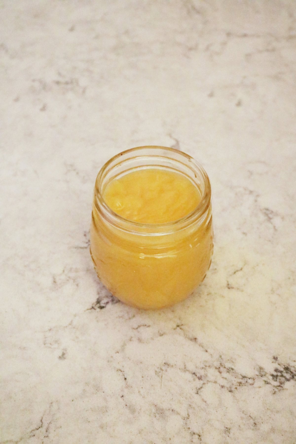 A jar of blood orange curd on a white marble counter top
