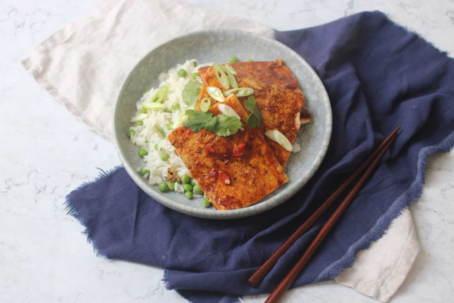A plate of soy glazed tofu served on top of white rice and peas