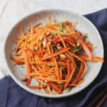 A plate of Soy and Ginger Carrot Salad on a light blue plate with a dark blue napkin
