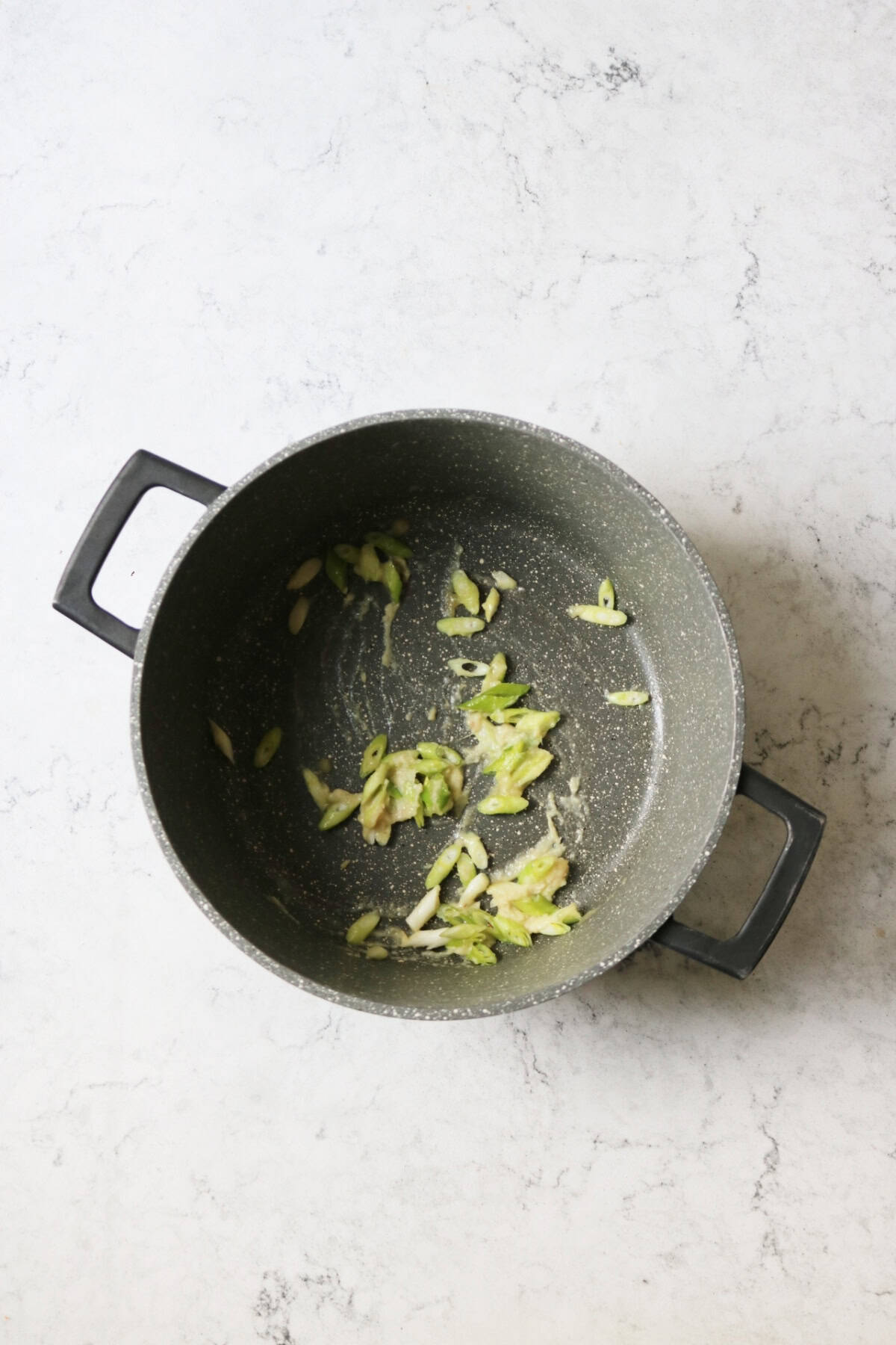 Sliced spring onions, ginger and garlic cooking in a large sauce pan