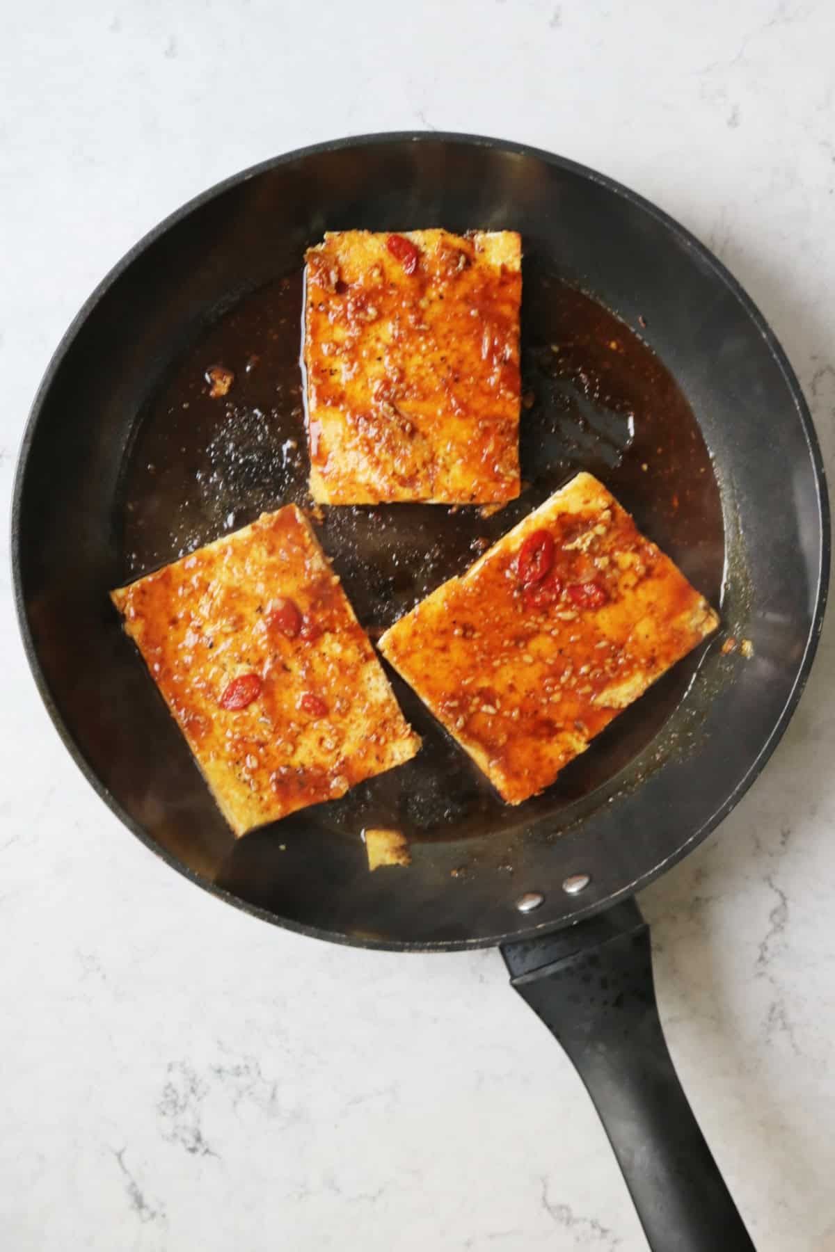Tofu with a soy glaze cooking in a large frying pan