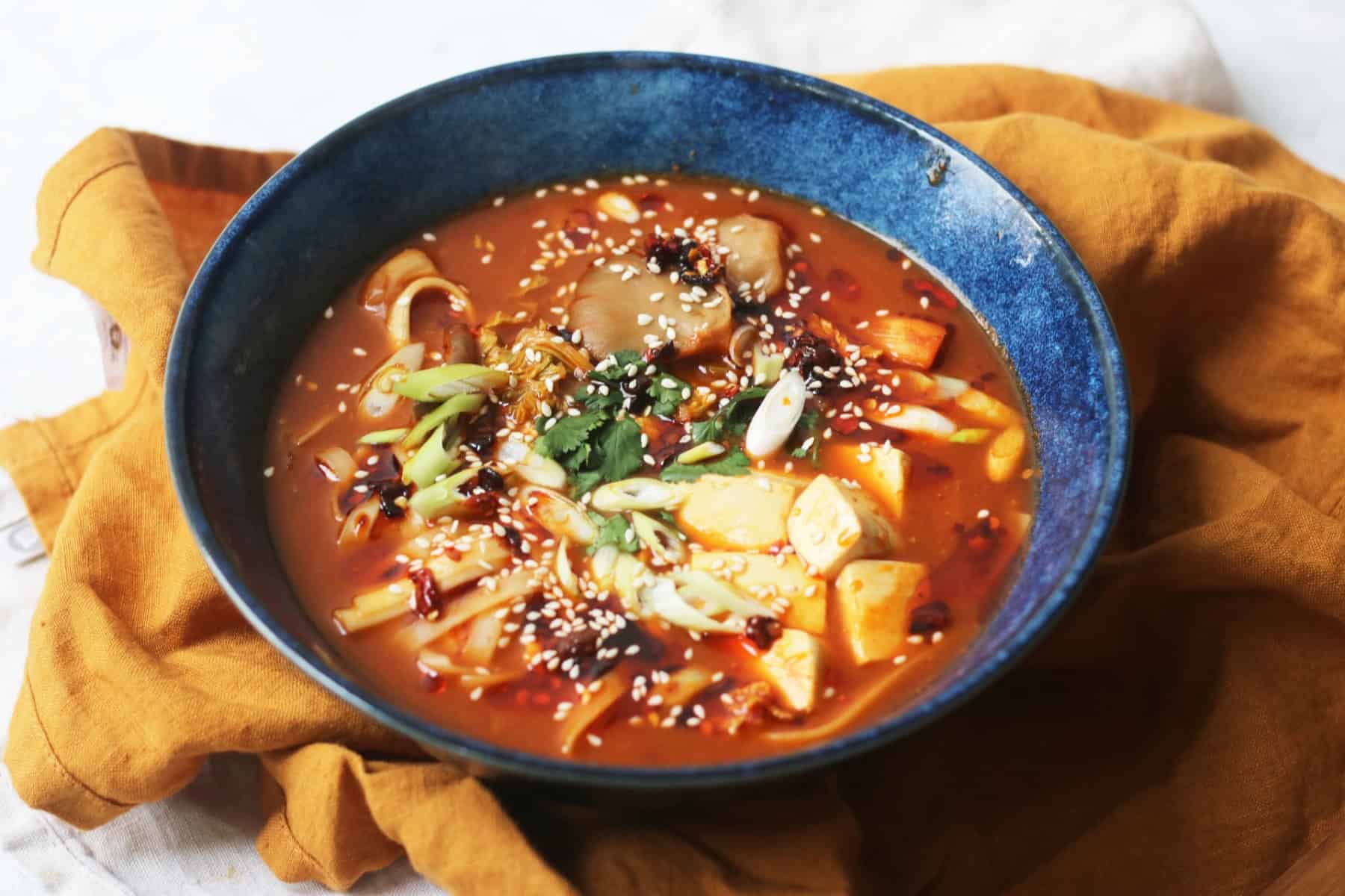 A bowl of Vegan Spicy Miso Ramen served in a blue bowl on top of a yellow napkin