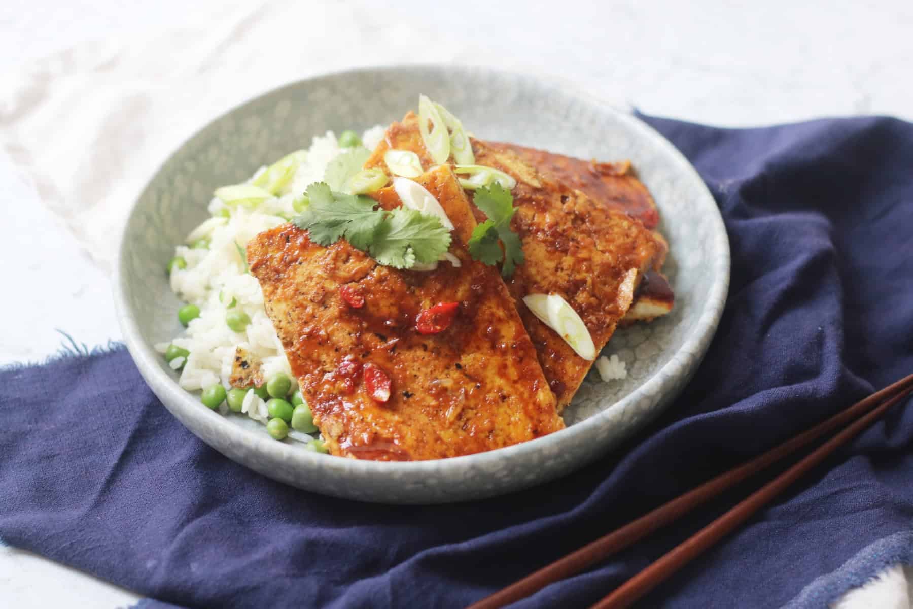 A plate of soy glazed tofu served on top of white rice and peas
