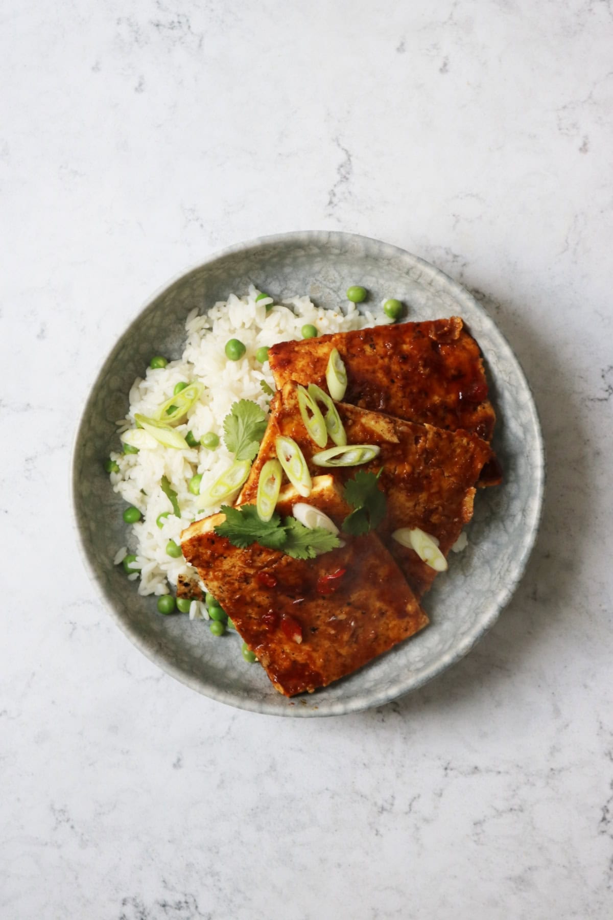 A plate of soy glazed tofu served on top of white rice and peas