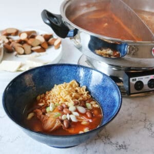 A bowl of Vegan Budae Jjigae next to an electronic hot pot
