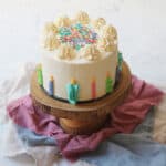 A vegan funfetti cake decorated with buttercream candles and sprinkles on a wooden cake stand