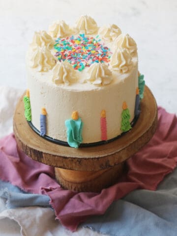 A vegan funfetti cake decorated with buttercream candles and sprinkles on a wooden cake stand