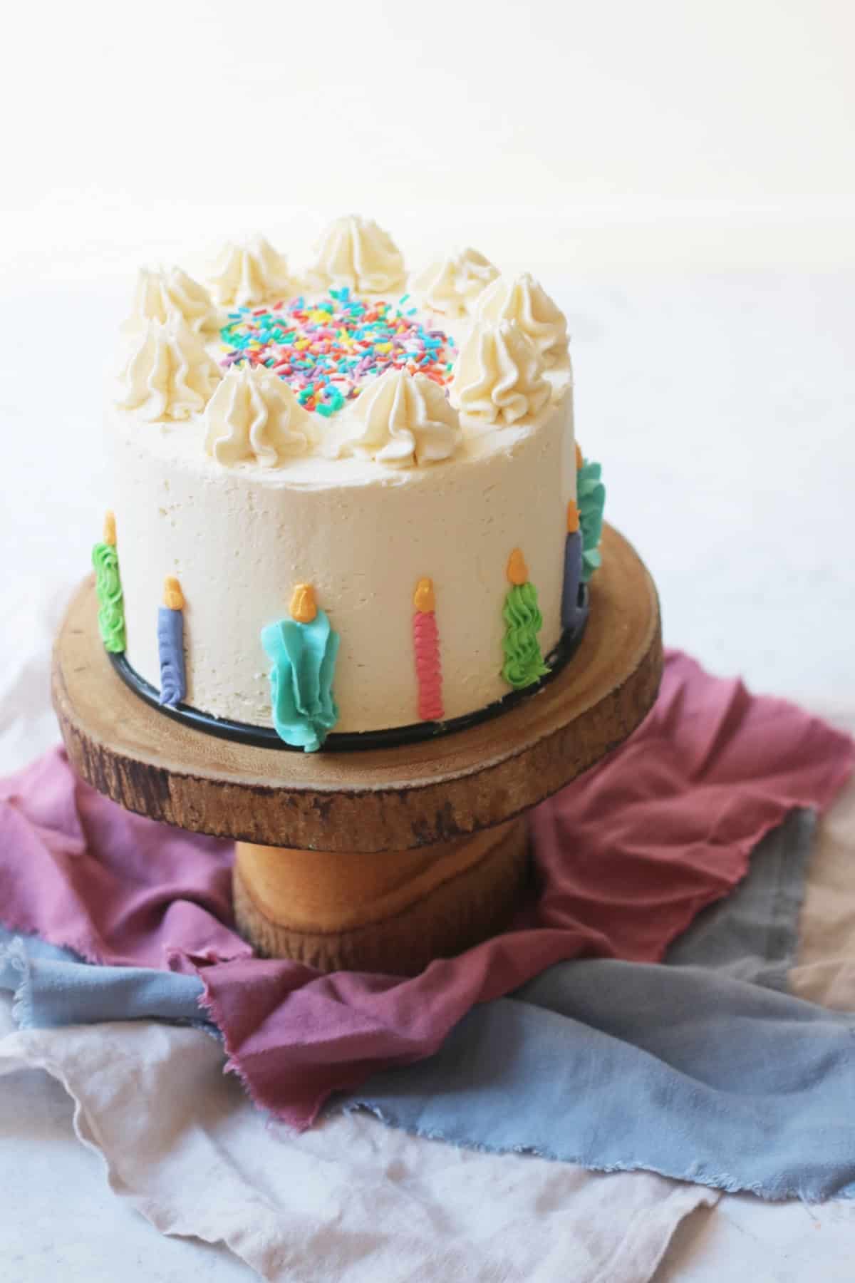 A vegan funfetti cake decorated with buttercream candles and sprinkles on a wooden cake stand