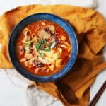 A bowl of Vegan Spicy Miso Ramen served in a blue bowl on top of a yellow napkin served alongside chopsticks and a spoon