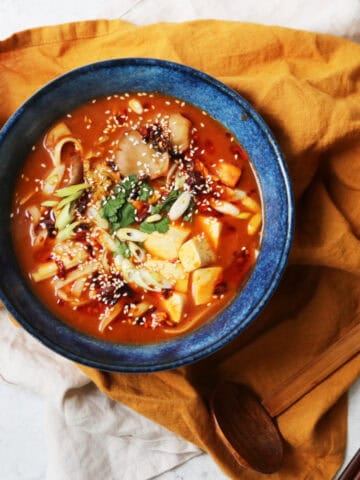 A bowl of Vegan Spicy Miso Ramen served in a blue bowl on top of a yellow napkin served alongside chopsticks and a spoon