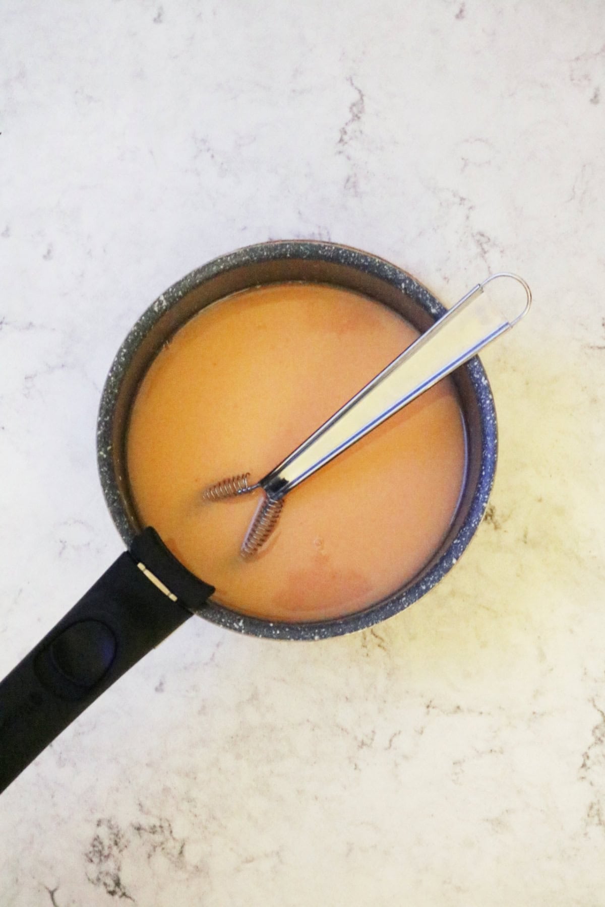 Warming the ingredients for blood orange curd in a sauce pan with a whisk