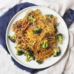 A plate of Vegan Broccoli and Mushroom Chow Mein on a dark blue napkin