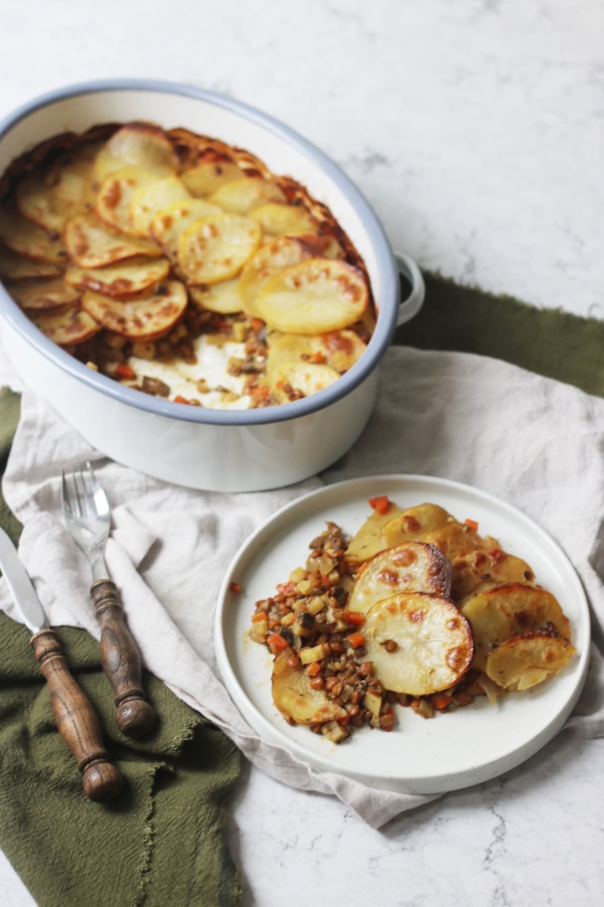 A plate of Vegan Lancashire Hot pot on a white and green napkin with a knife and fork that have a wooden handle