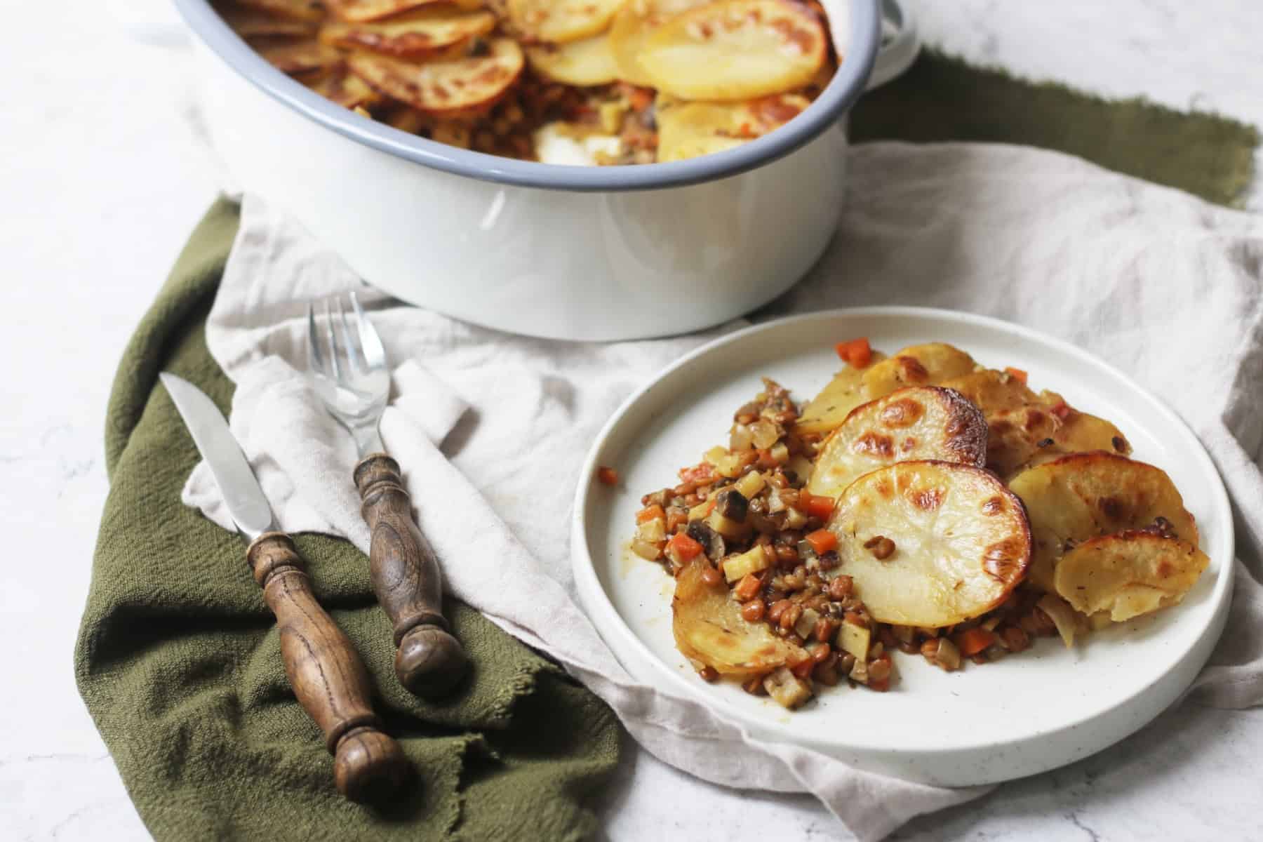 A plate of Vegan Lancashire Hot pot on a white and green napkin with a knife and fork that have a wooden handle