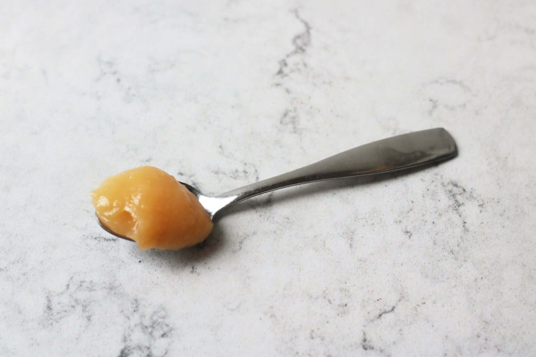 A spoon of Vegan Blood Orange Curd resting on a white marble counter top