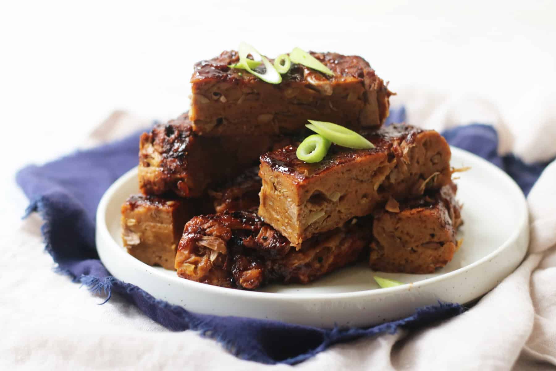 Vegan Chinese Spare Ribs stacked high on a plate with a dark blue napkin