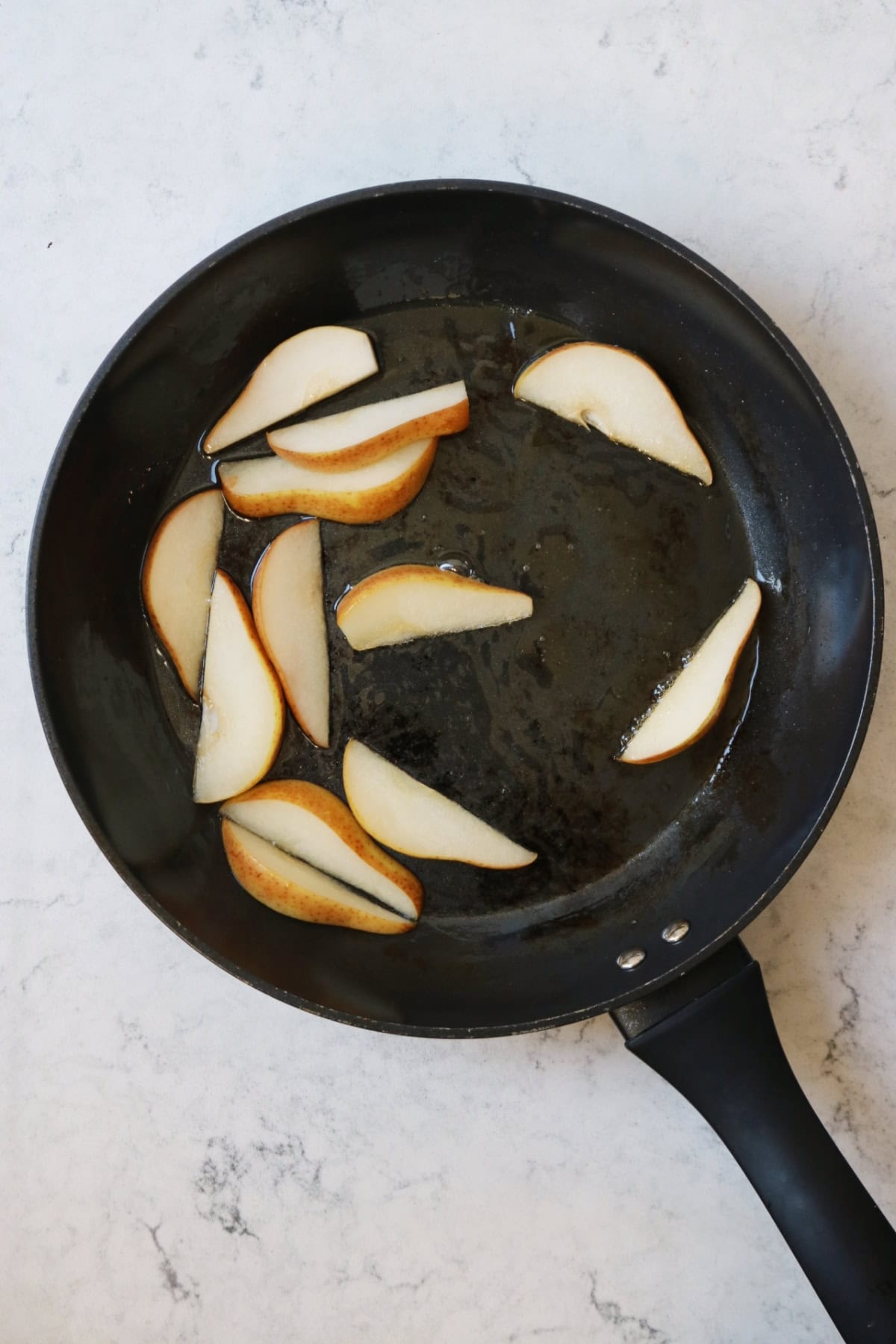 Slices of pear caramelising in a syrup of water and maple syrup in a large flat bottomed pan.