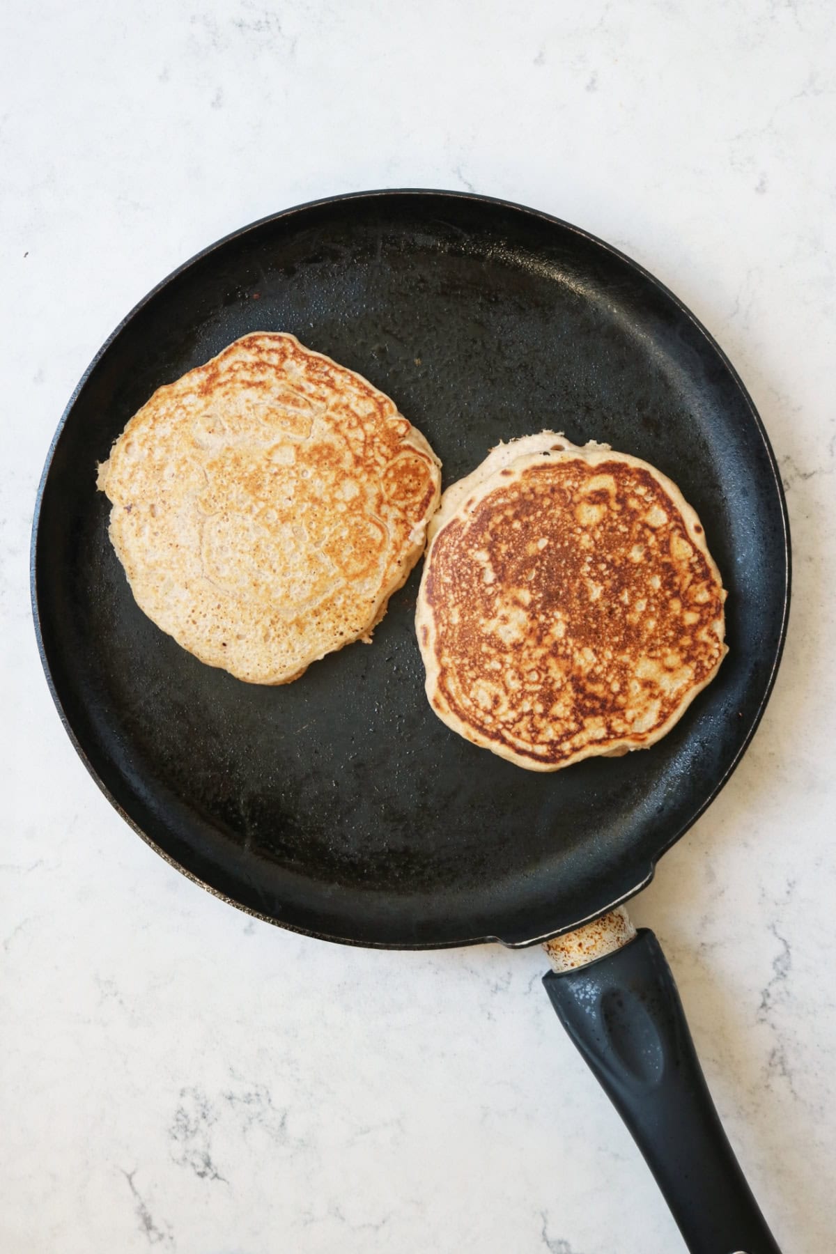 2 vegan pear and ginger pancakes that are cooked on one side being heated on a large crepe pan.