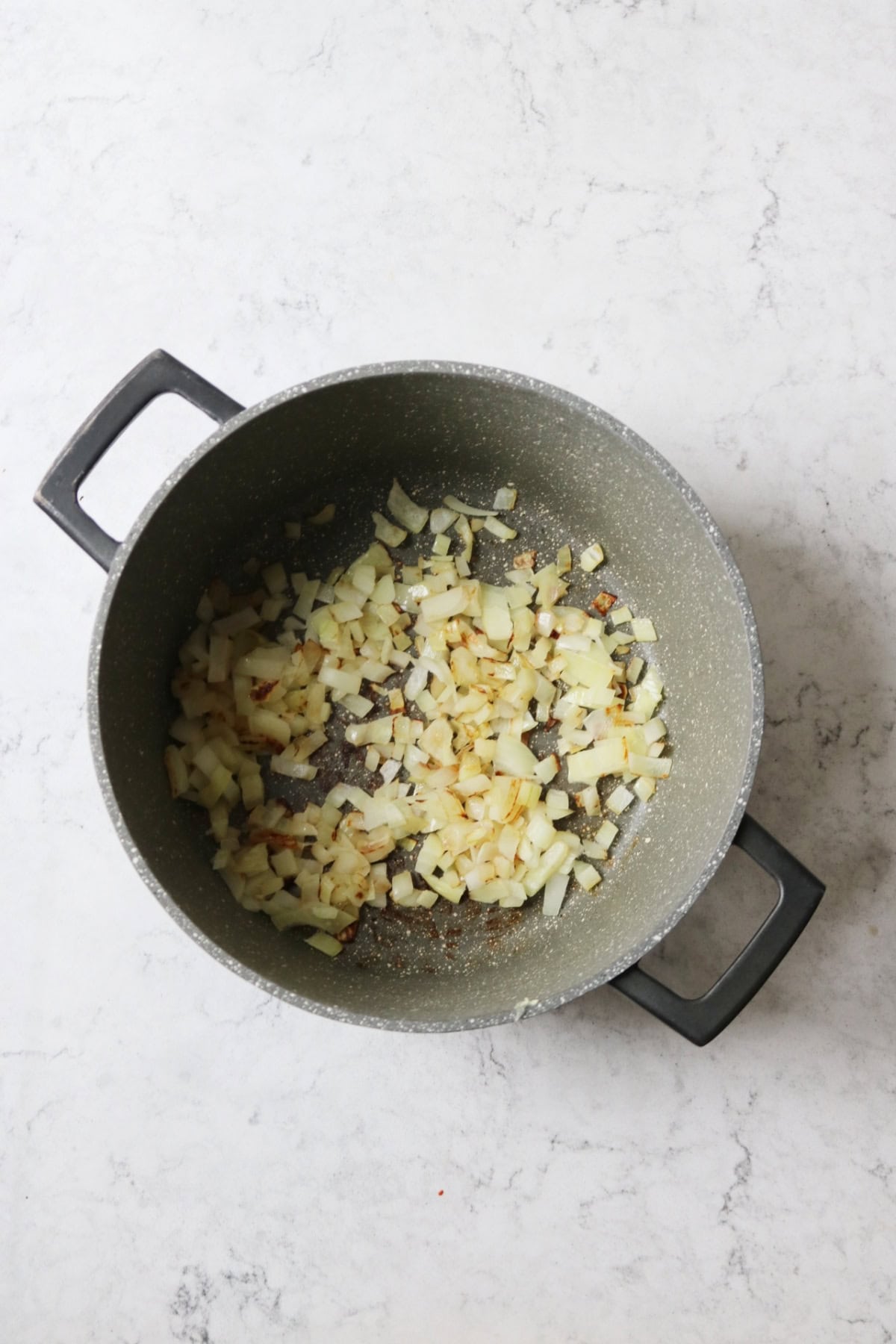 Diced white onion cooking in a large sauce pan
