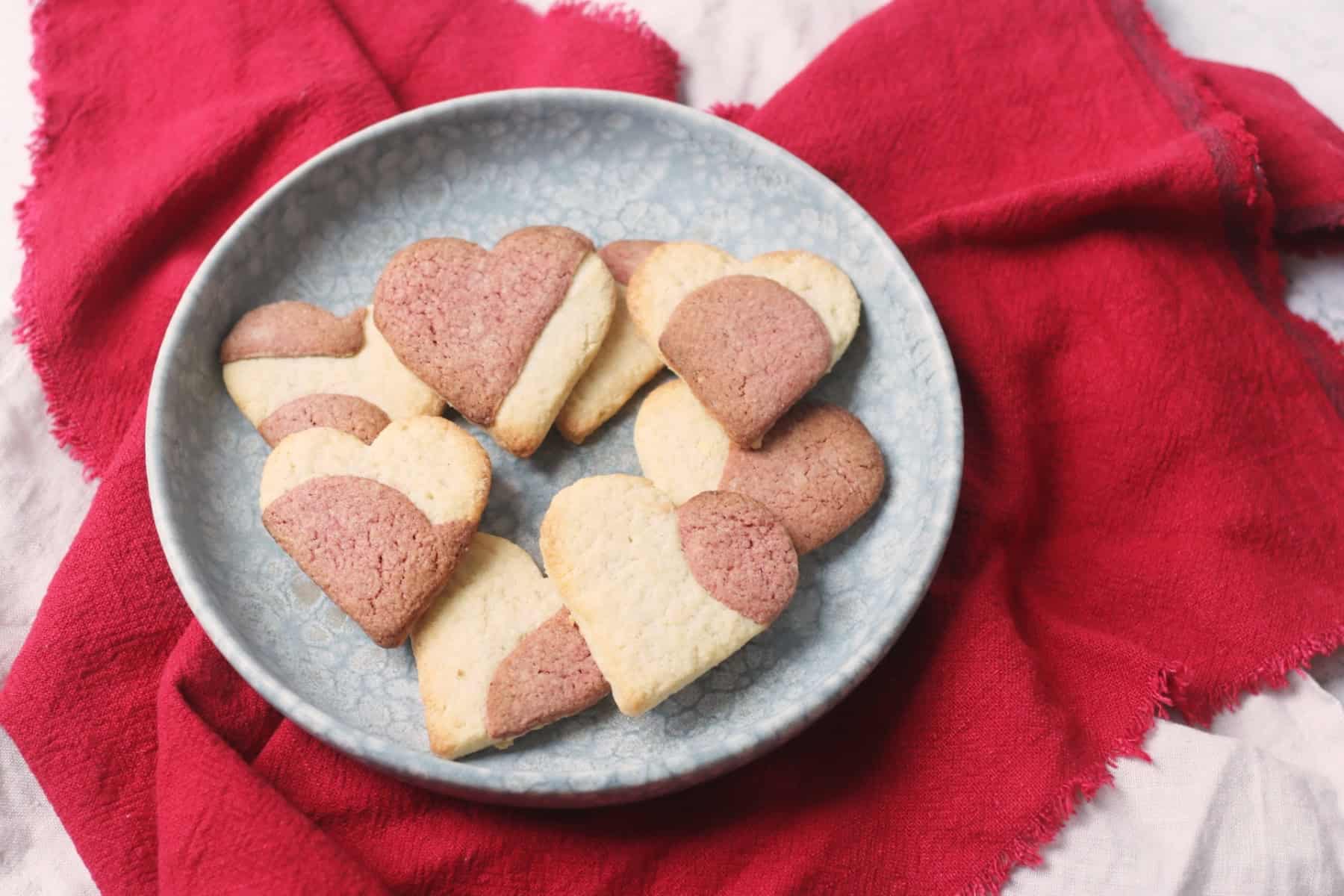 Vegan Heart Shaped Strawberry Sugar Cookies on a blue plate on top of a red napkin