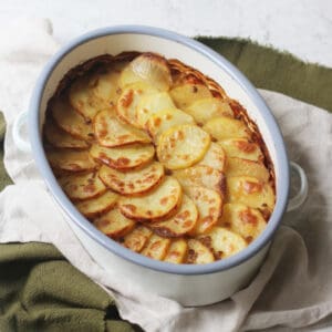 A Vegan Lancashire Hot Pot with crispy potato slices on top in an enamel oven dish placed on top of a green and white napkin