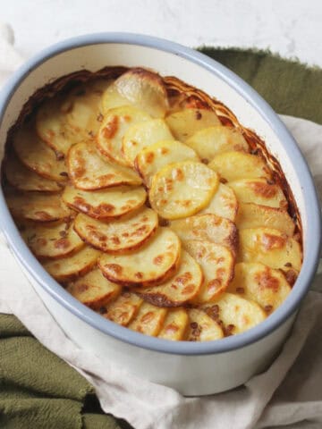 A Vegan Lancashire Hot Pot with crispy potato slices on top in an enamel oven dish placed on top of a green and white napkin