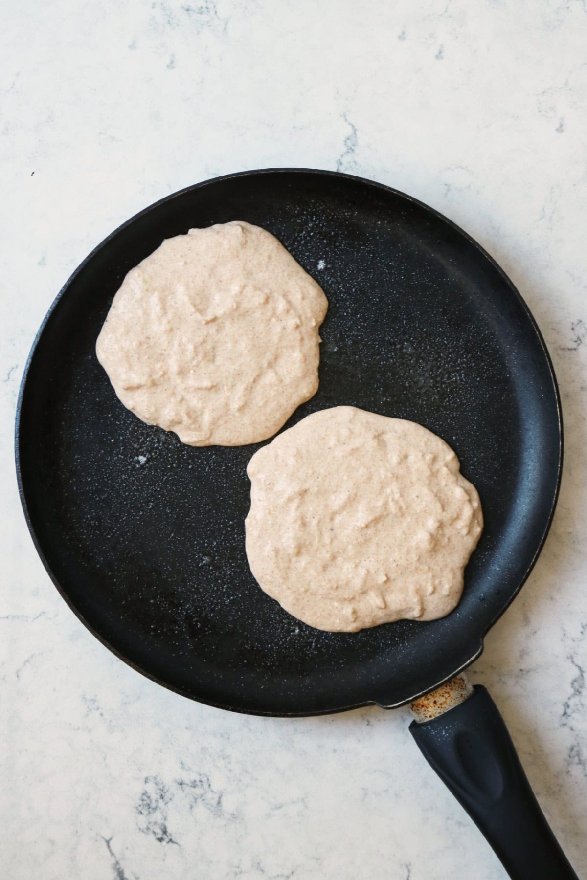 2 uncooked vegan pear and ginger pancakes being heated on a large crepe pan.