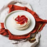 Vegan Blood Orange Pavlova on a white plate with orange napkin and gold spoon
