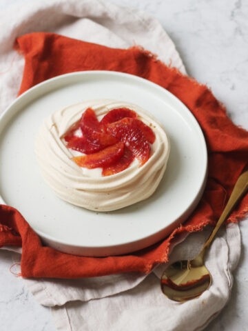 Vegan Blood Orange Pavlova on a white plate with orange napkin and gold spoon