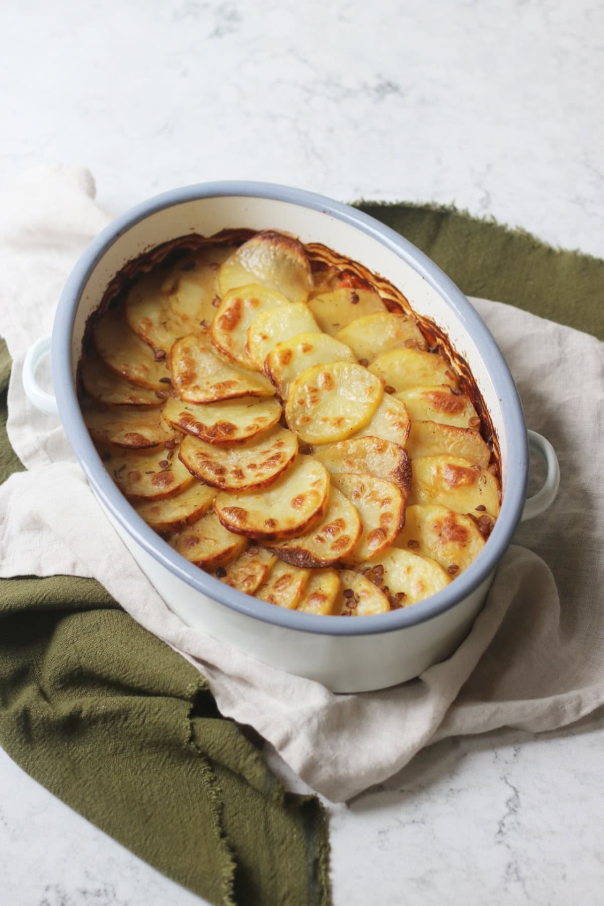 A Vegan Lancashire Hot Pot with crispy potato slices on top in an enamel oven dish placed on top of a green and white napkin