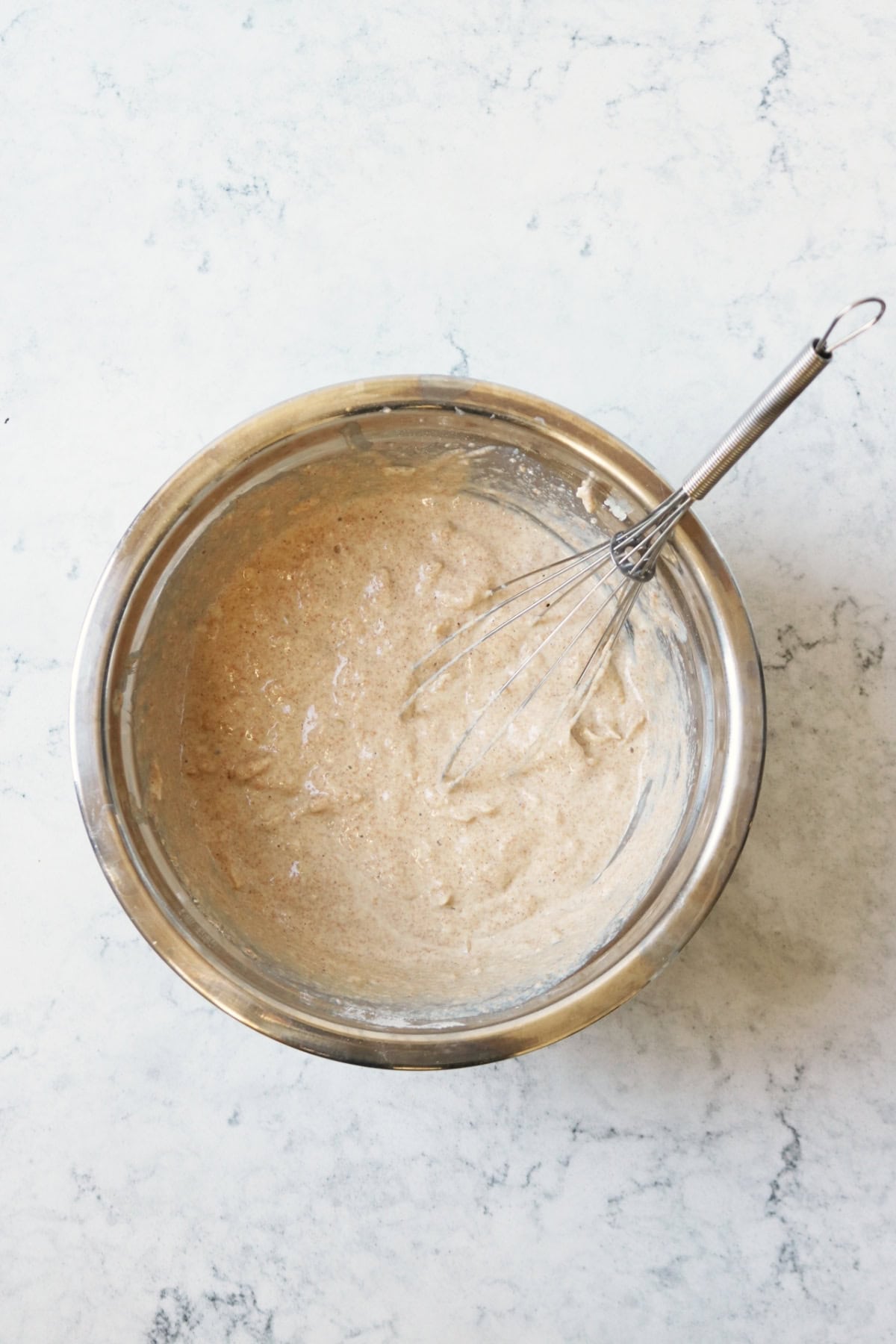 Pancake batter for vegan pear and ginger pancakes that has been mixed together in a metal bowl with a metal whisk.